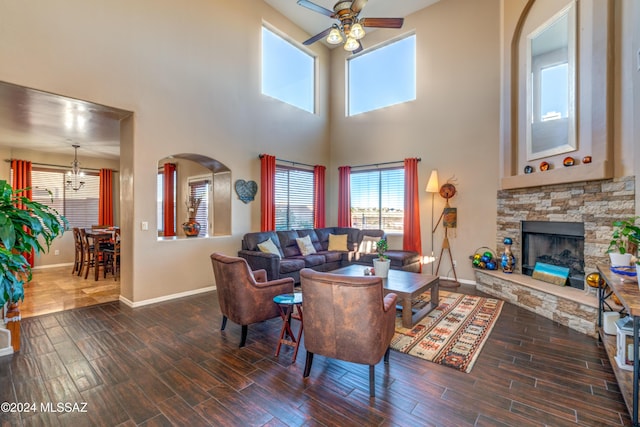 living room featuring ceiling fan with notable chandelier, wood finish floors, a fireplace, and baseboards