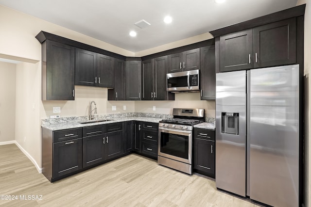 kitchen with light stone counters, sink, stainless steel appliances, and light hardwood / wood-style flooring