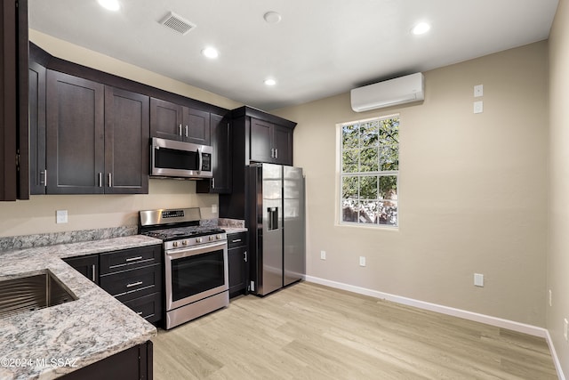 kitchen featuring light stone counters, light hardwood / wood-style flooring, appliances with stainless steel finishes, and a wall mounted AC