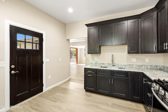 kitchen with light stone counters, sink, light hardwood / wood-style floors, and stainless steel range oven