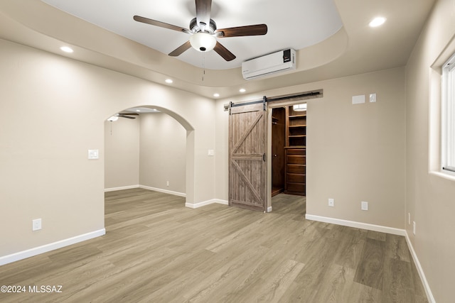 spare room with wood-type flooring, a barn door, an AC wall unit, and ceiling fan