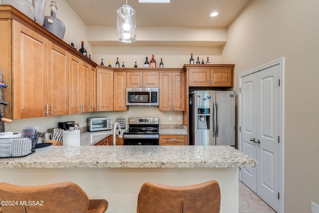 kitchen with kitchen peninsula, appliances with stainless steel finishes, a kitchen bar, and hanging light fixtures