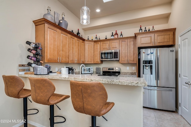 kitchen featuring kitchen peninsula, light stone countertops, light tile patterned floors, appliances with stainless steel finishes, and a breakfast bar area