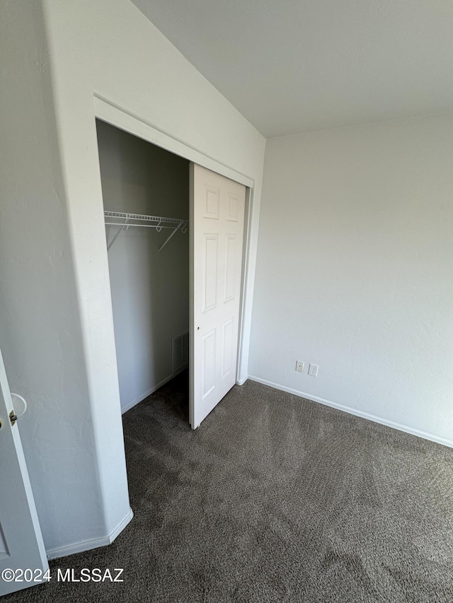 unfurnished bedroom featuring dark carpet and a closet