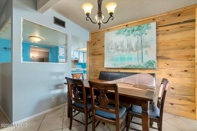 dining area featuring wood walls, light tile patterned flooring, a chandelier, and a textured ceiling