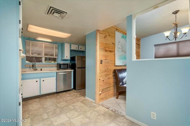 kitchen with sink, a notable chandelier, wood walls, pendant lighting, and appliances with stainless steel finishes