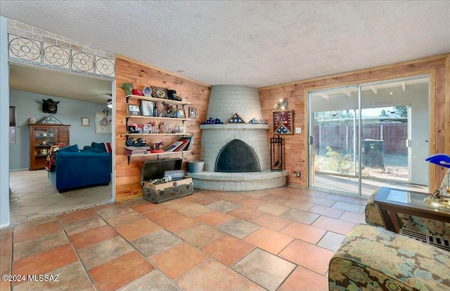 living room with a fireplace, a textured ceiling, ceiling fan, and wood walls