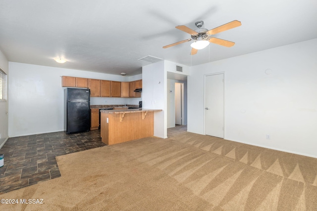 kitchen featuring a breakfast bar, dark colored carpet, black refrigerator, kitchen peninsula, and ceiling fan