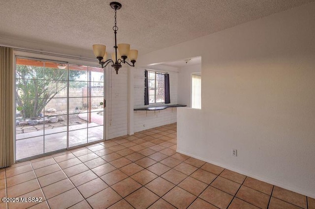 unfurnished dining area with a notable chandelier, light tile patterned floors, and a textured ceiling