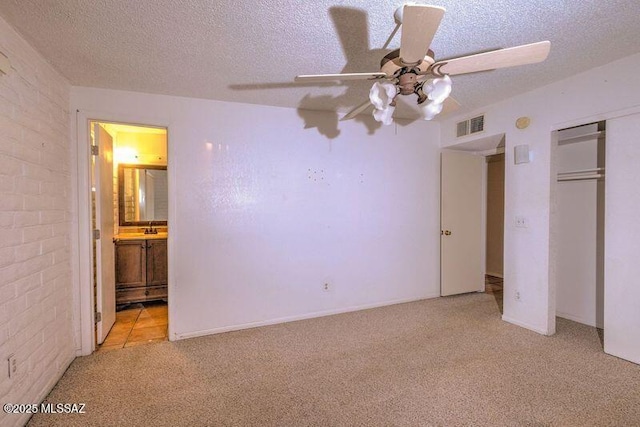 unfurnished bedroom with ceiling fan, ensuite bathroom, a textured ceiling, light carpet, and a closet