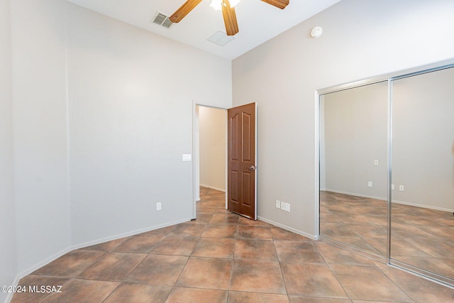 unfurnished bedroom with dark tile patterned floors, a closet, high vaulted ceiling, and ceiling fan