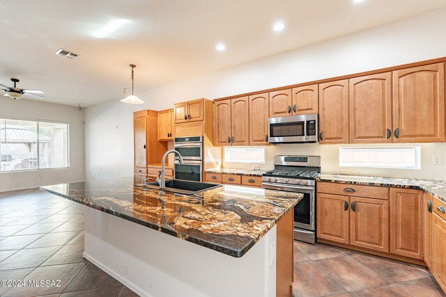 kitchen featuring sink, stainless steel appliances, an island with sink, pendant lighting, and dark tile patterned flooring