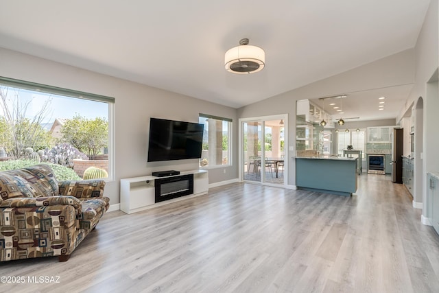 living room featuring baseboards, light wood-style flooring, vaulted ceiling, and beverage cooler