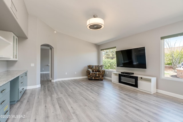unfurnished living room featuring light wood-style flooring, arched walkways, and baseboards