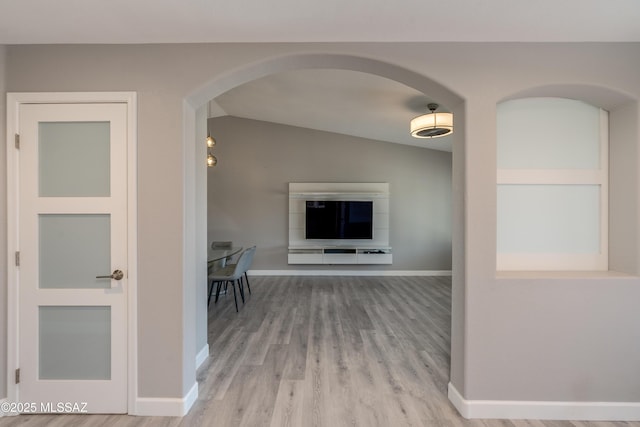 corridor with arched walkways, baseboards, lofted ceiling, and wood finished floors