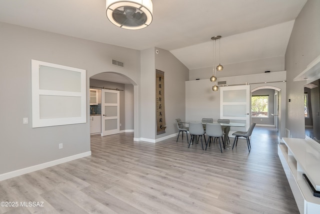dining room with arched walkways, a barn door, wood finished floors, and vaulted ceiling
