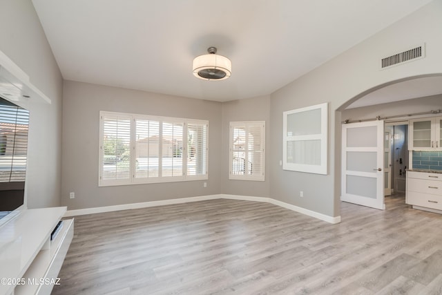 unfurnished living room featuring arched walkways, baseboards, light wood-style floors, and visible vents