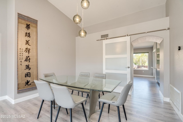 dining area featuring arched walkways, lofted ceiling, visible vents, and light wood-type flooring