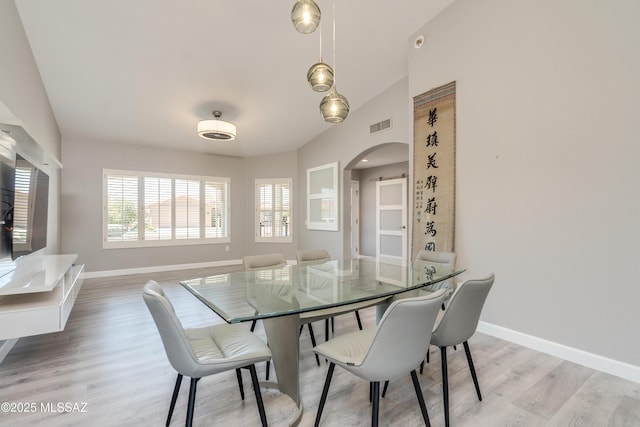 dining area with arched walkways, baseboards, light wood finished floors, and visible vents