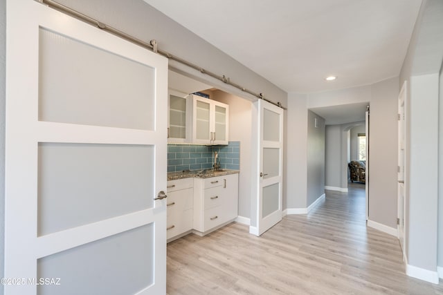 hallway featuring a barn door, light wood-style flooring, baseboards, and recessed lighting