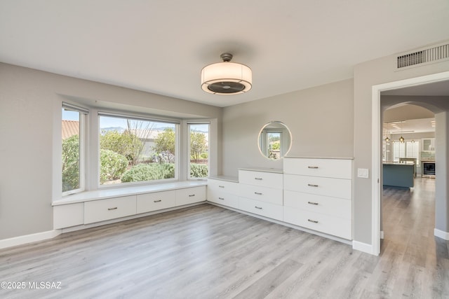 unfurnished bedroom featuring baseboards, visible vents, light wood-style flooring, and arched walkways