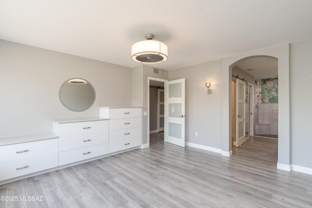 unfurnished bedroom featuring arched walkways, visible vents, baseboards, and light wood-style floors
