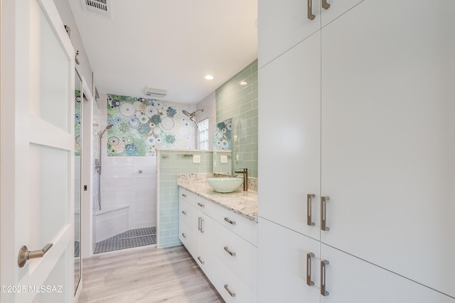full bath featuring vanity, tile walls, a stall shower, visible vents, and wood finished floors