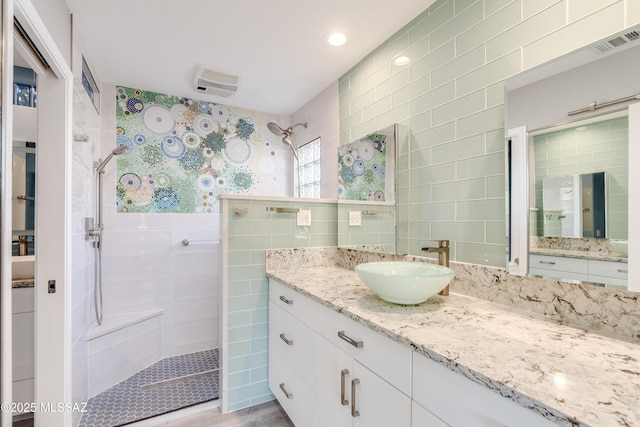 full bath featuring visible vents, vanity, tile walls, and walk in shower