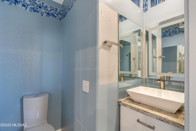 bathroom with a textured wall, toilet, vanity, and backsplash