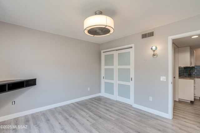 unfurnished room featuring light wood-style floors, a sink, baseboards, and visible vents