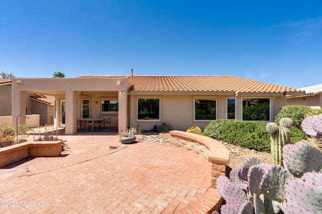 rear view of property with outdoor dining area, ceiling fan, a tile roof, stucco siding, and a patio area