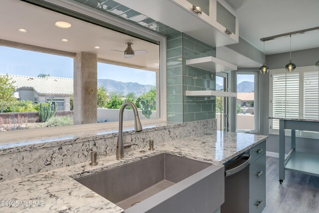 kitchen with a sink, a mountain view, light stone counters, dishwashing machine, and wood finished floors