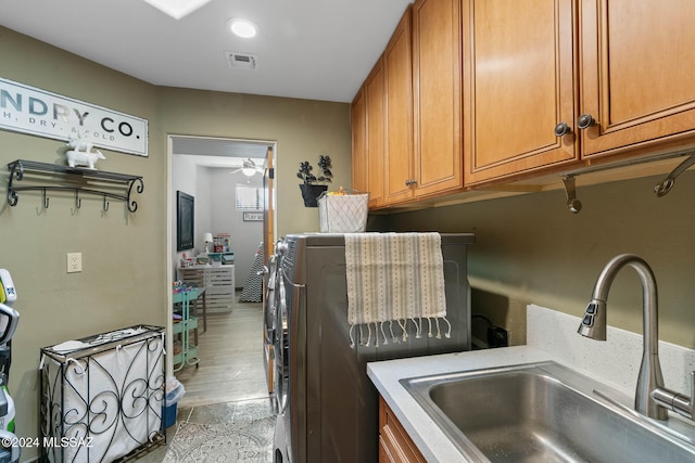 clothes washing area with cabinets, washing machine and clothes dryer, sink, and light hardwood / wood-style flooring