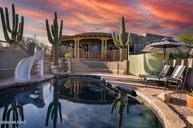 pool at dusk with a patio area and a water slide