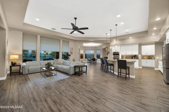 living room featuring ceiling fan, wood-type flooring, and a tray ceiling