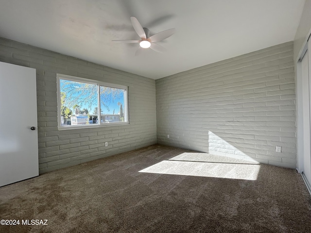 unfurnished room featuring ceiling fan, brick wall, and dark colored carpet