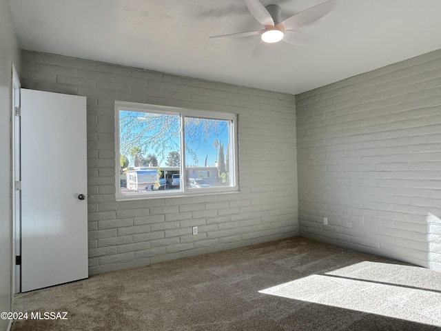 carpeted spare room featuring ceiling fan and brick wall