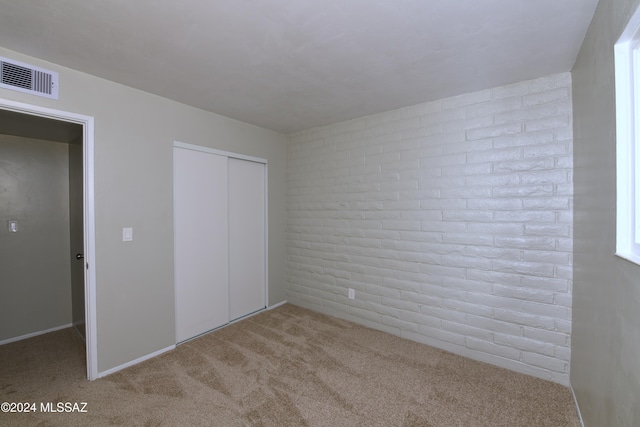 unfurnished bedroom with light carpet, a closet, and brick wall