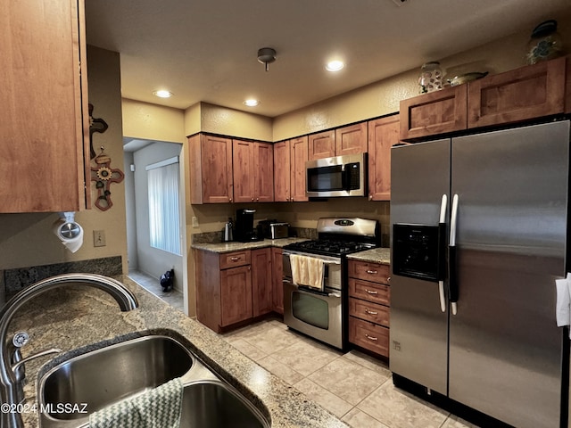 kitchen with stainless steel appliances, light stone countertops, sink, and light tile patterned floors