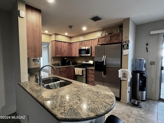 kitchen with appliances with stainless steel finishes, kitchen peninsula, sink, and light stone countertops