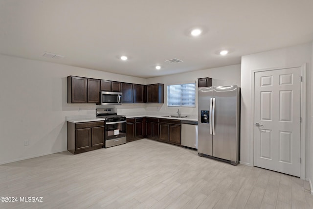 kitchen with dark brown cabinetry, stainless steel appliances, light hardwood / wood-style floors, and sink