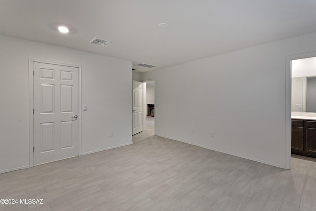 unfurnished bedroom featuring ensuite bathroom and light hardwood / wood-style flooring