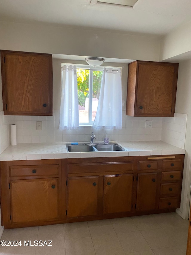 kitchen featuring tile countertops, brown cabinetry, a sink, and decorative backsplash