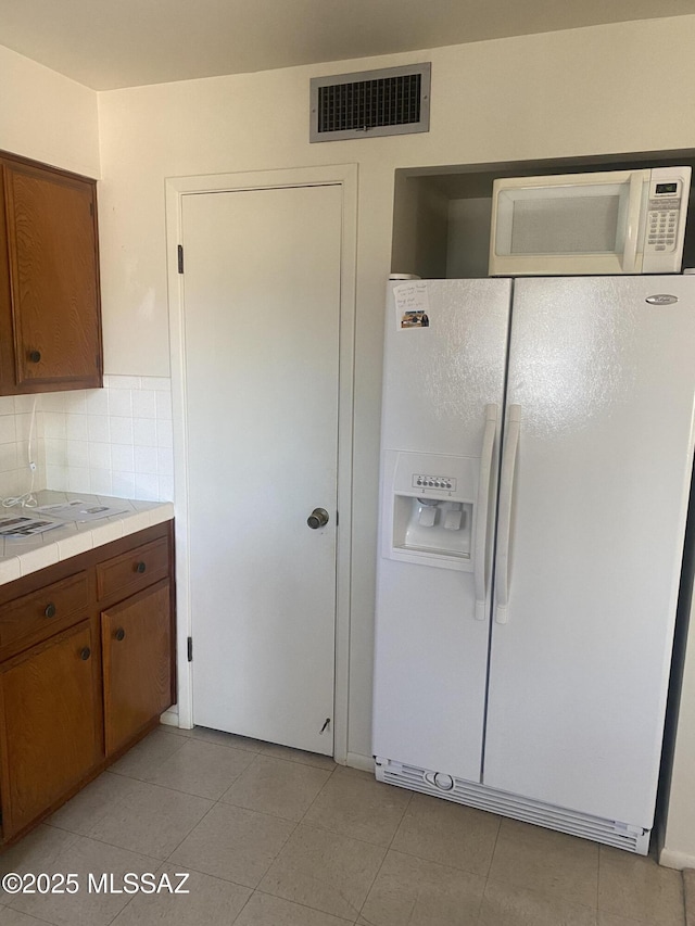 kitchen featuring tile countertops, white appliances, visible vents, brown cabinets, and decorative backsplash