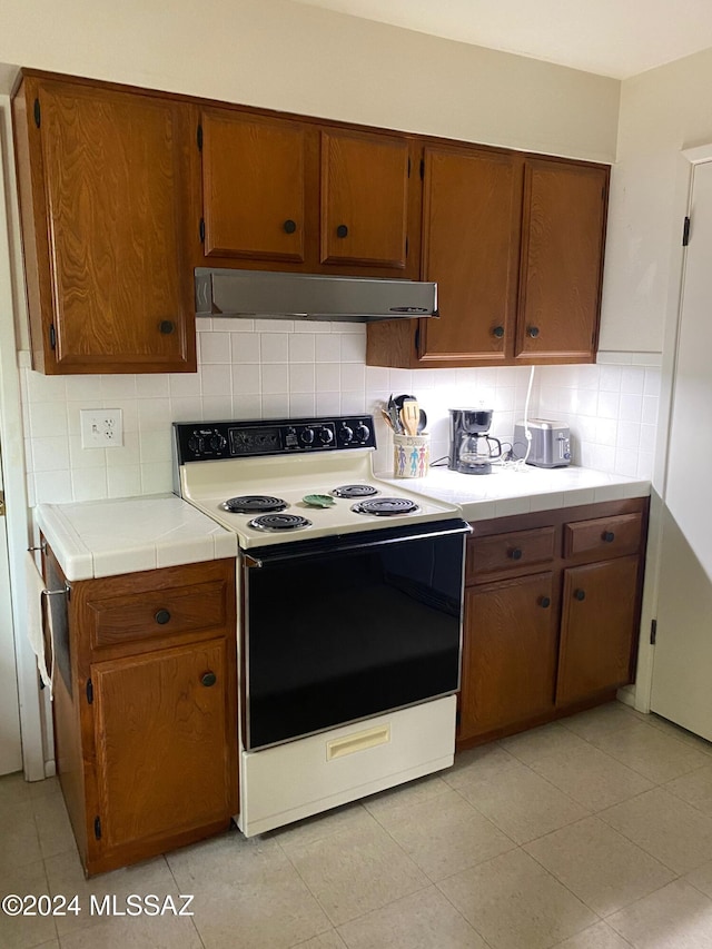 kitchen with tile counters, light tile patterned flooring, electric stove, and backsplash