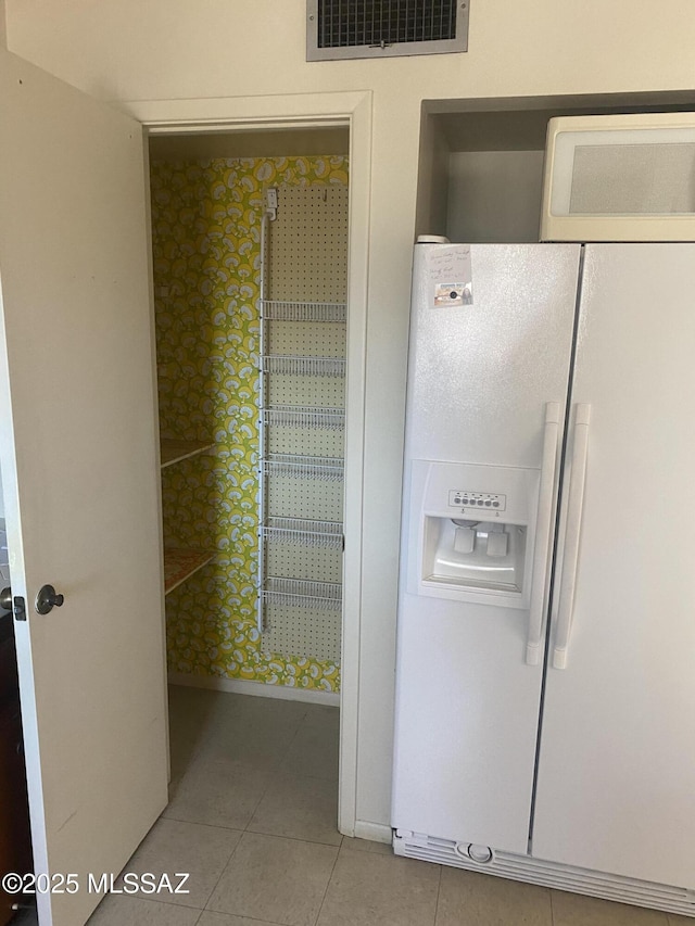 kitchen featuring light tile patterned floors, white refrigerator with ice dispenser, visible vents, and baseboards