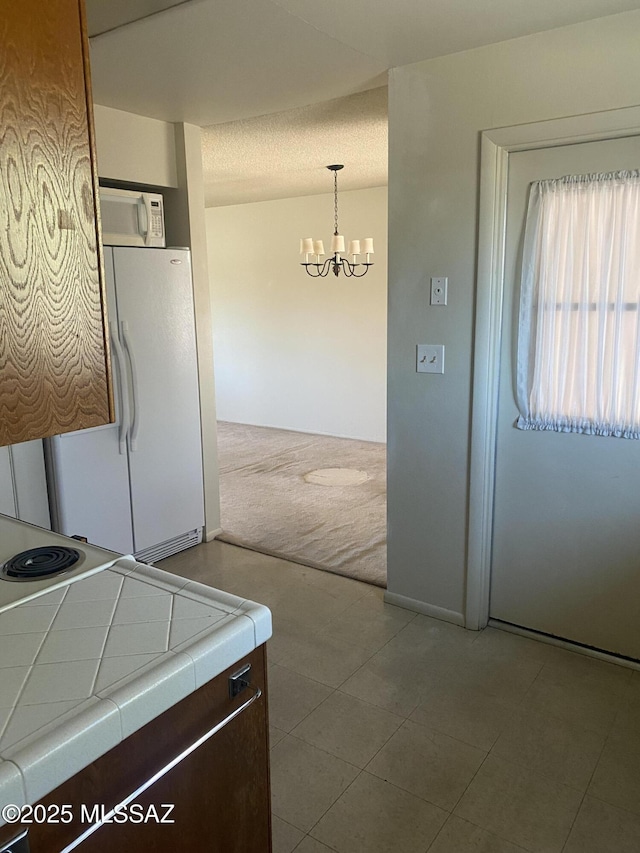 kitchen with white appliances, tile counters, hanging light fixtures, carpet, and a notable chandelier