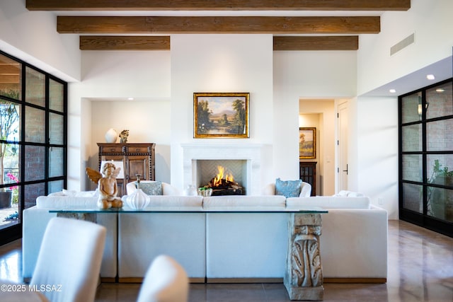 5200 N Camino Antonio, Tucson, AZ 85718 - living area featuring a warm lit fireplace, beamed ceiling, concrete floors, visible vents, and a towering ceiling
