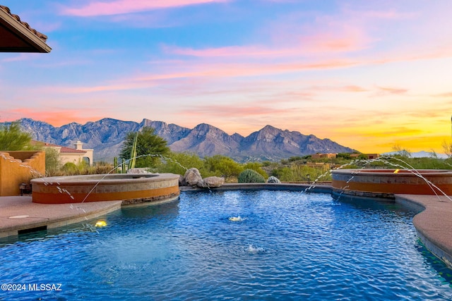 pool at dusk featuring a mountain view and pool water feature