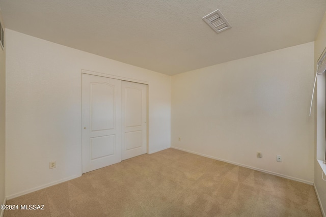 unfurnished bedroom featuring a textured ceiling, light colored carpet, and a closet